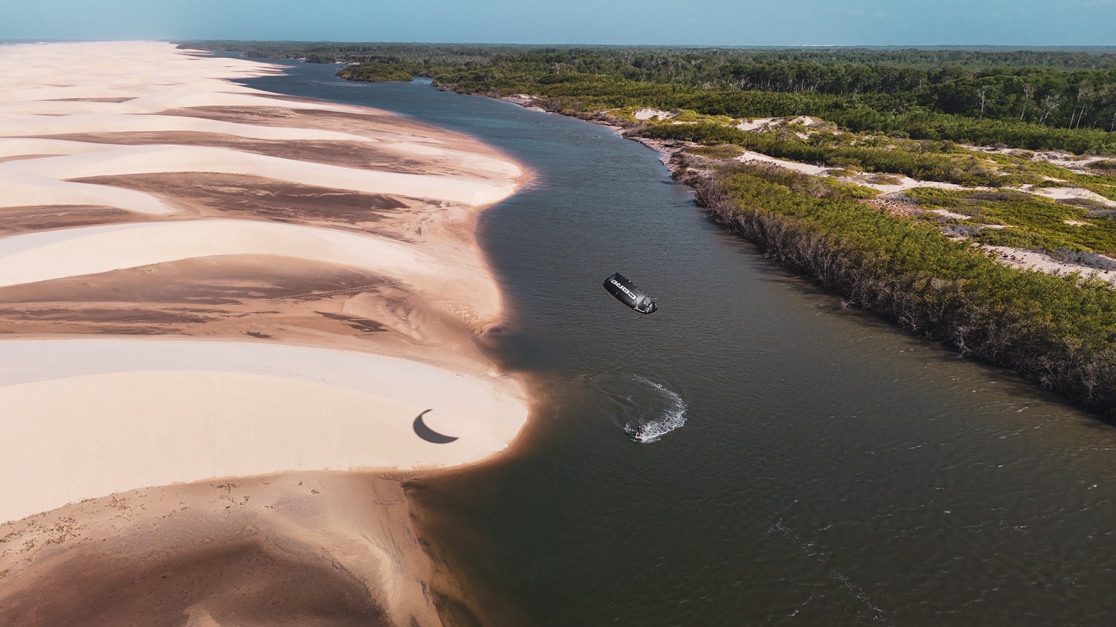 Aerial drone view of a kitesurfer riding the river between white sand dunes and mangroves near Atins, Lençóis Maranhenses, Brazil — Local Secrets XP