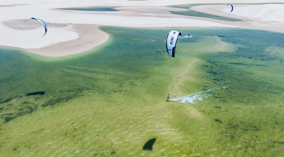 Aerial view of kitesurfers in crystal-clear green lagoon with white sand channels — Lençóis Maranhenses, Brazil