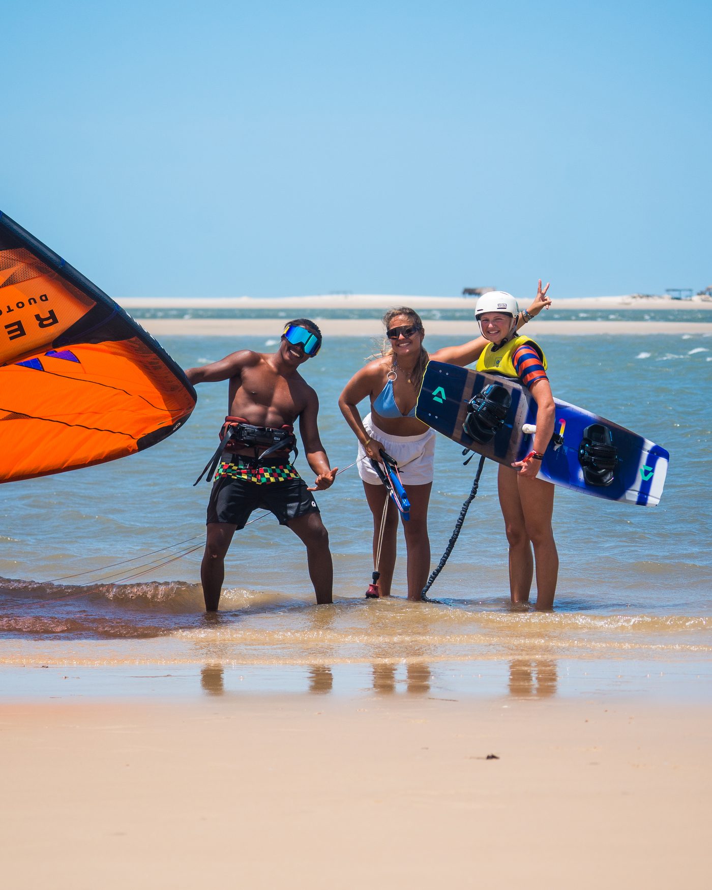 Trois kitesurfeurs sur un banc de sable à Atins, Lençóis Maranhenses, Brésil, l'un tenant une aile orange et l'autre une planche twin-tip — un trip kitesurf en petit groupe avec Local Secrets XP