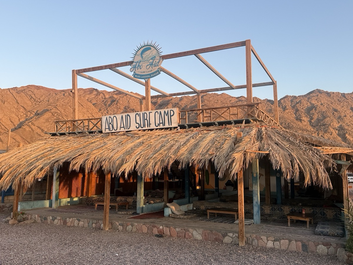 Abo Aid Surf Camp thatched entrance with golden Sinai mountains at sunset — Dahab
