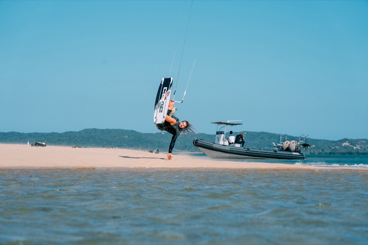 Kitesurfer performing inverted big-air trick over Inhaca Island sandbar with support RIB boat — Mozambique expedition