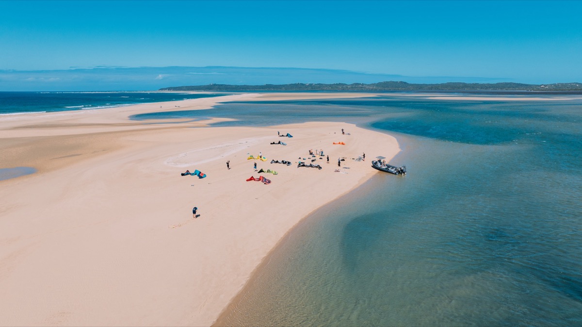 Drone view of kitesurfing session on pristine Inhaca Island sandbar with colorful kites and RIB support boat
